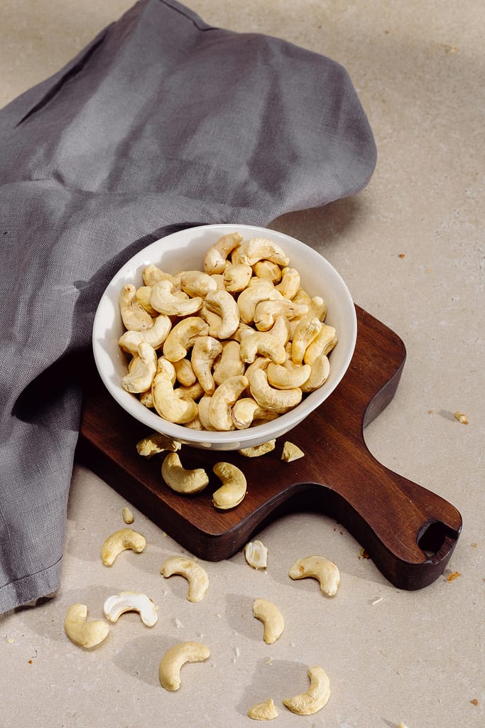 Top view of cashew nuts in a bowl on a wooden cutting board, perfect for healthy snack concepts.
